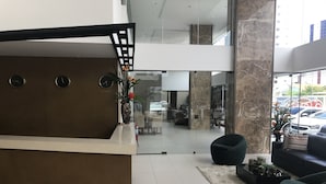 Een moderne receptie met een receptiebalie, een glazen scheiding en een zithoek met een bank en stoelen.
