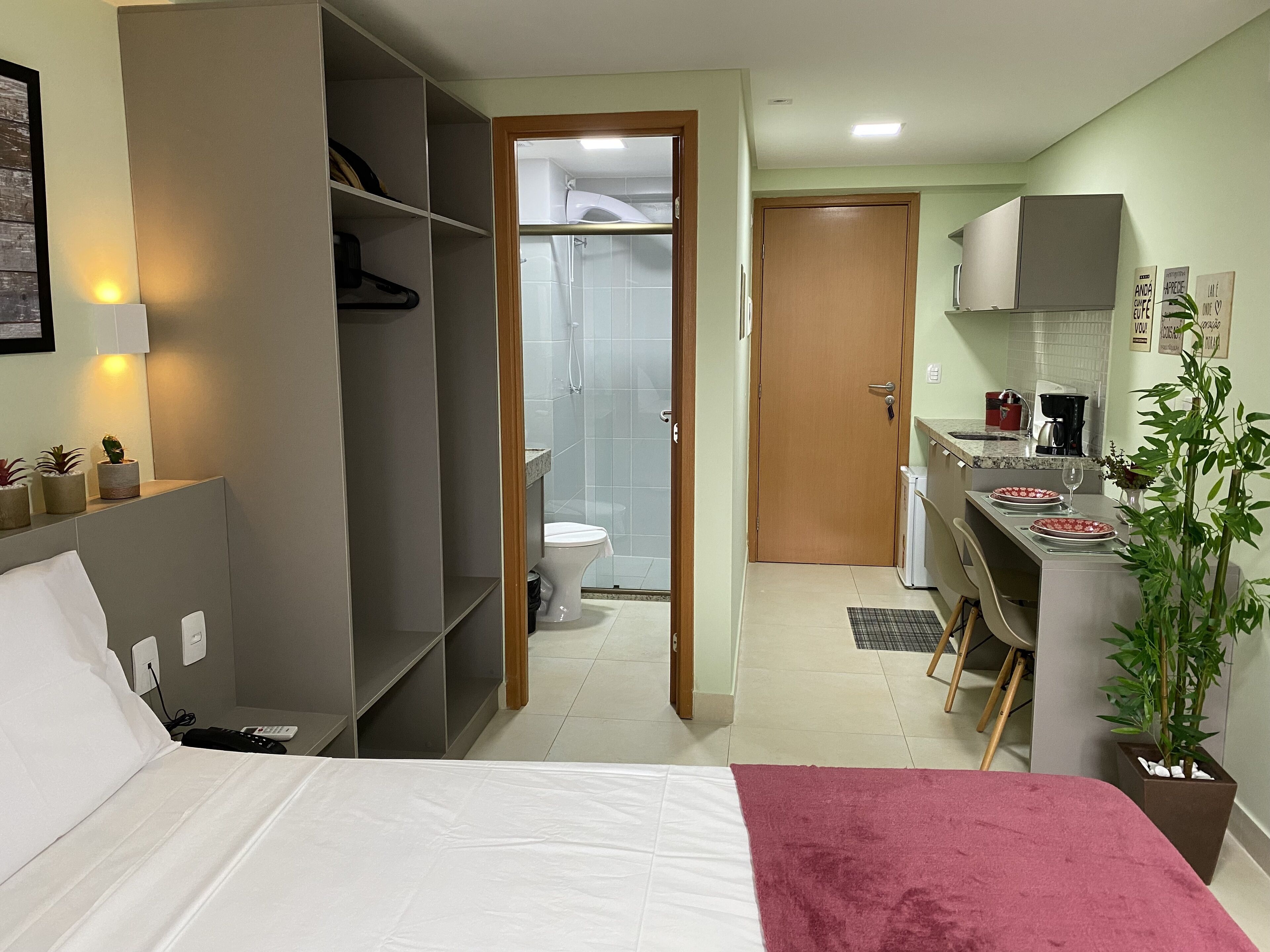 A compact hotel room with a bed, a small kitchenette, a bathroom with a shower, and a closet.