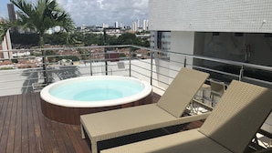 Een terras op het dak met een jacuzzi, lounge stoelen en uitzicht over de stad.