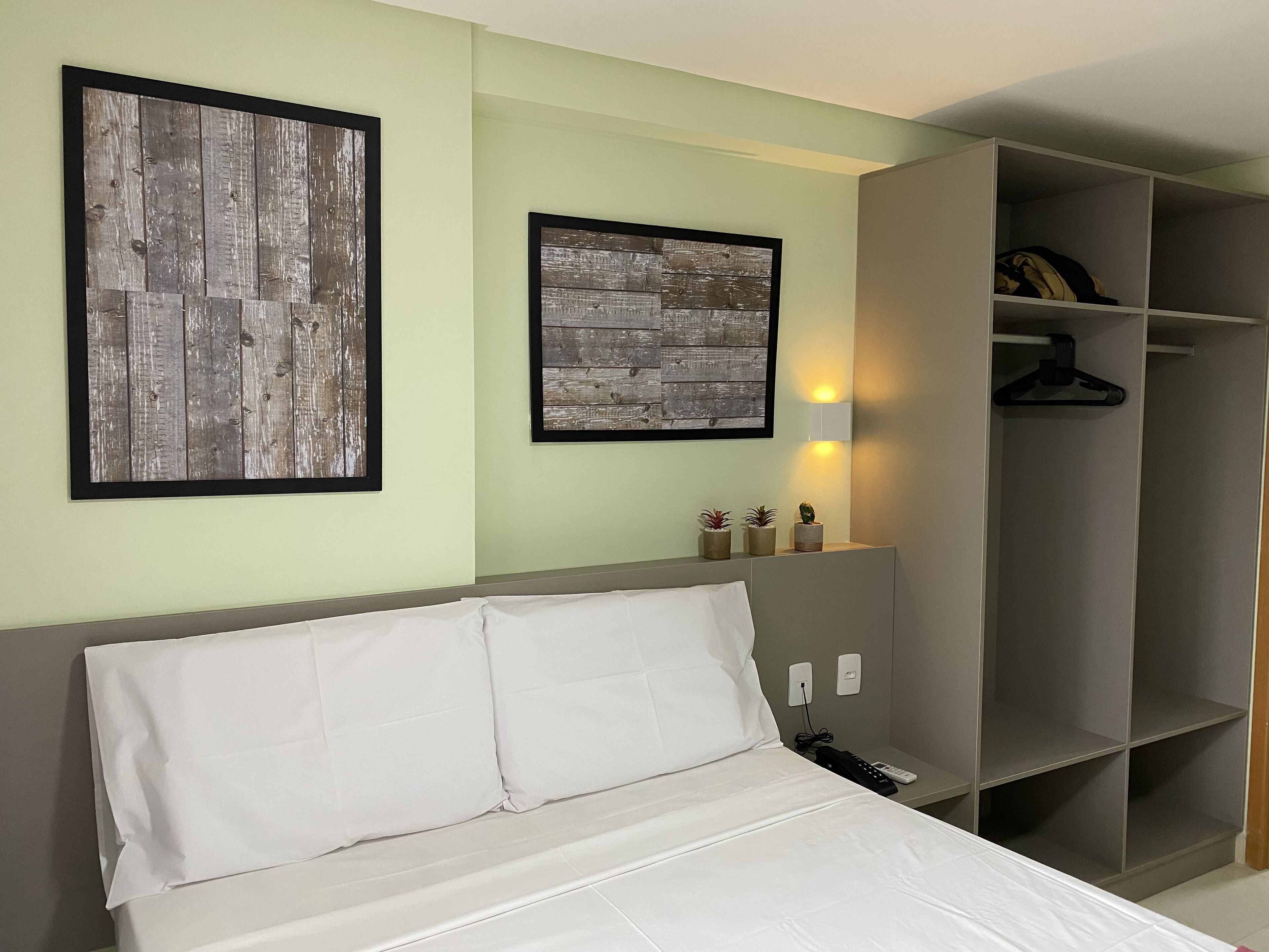 A neatly arranged bedroom with a bed, a wardrobe, and two framed pictures on the wall.