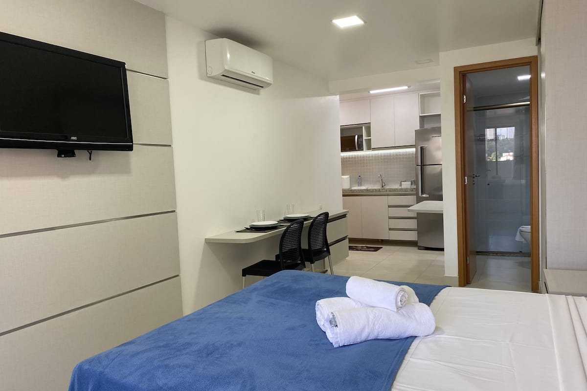 Una habitación de hotel con cama, escritorio, silla, televisor de pantalla plana y kitchenette.