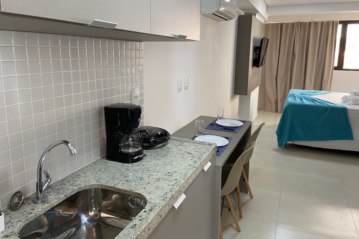 Una habitación de hotel compacta con kitchenette, una cama con cubierta azul y un baño con ducha.