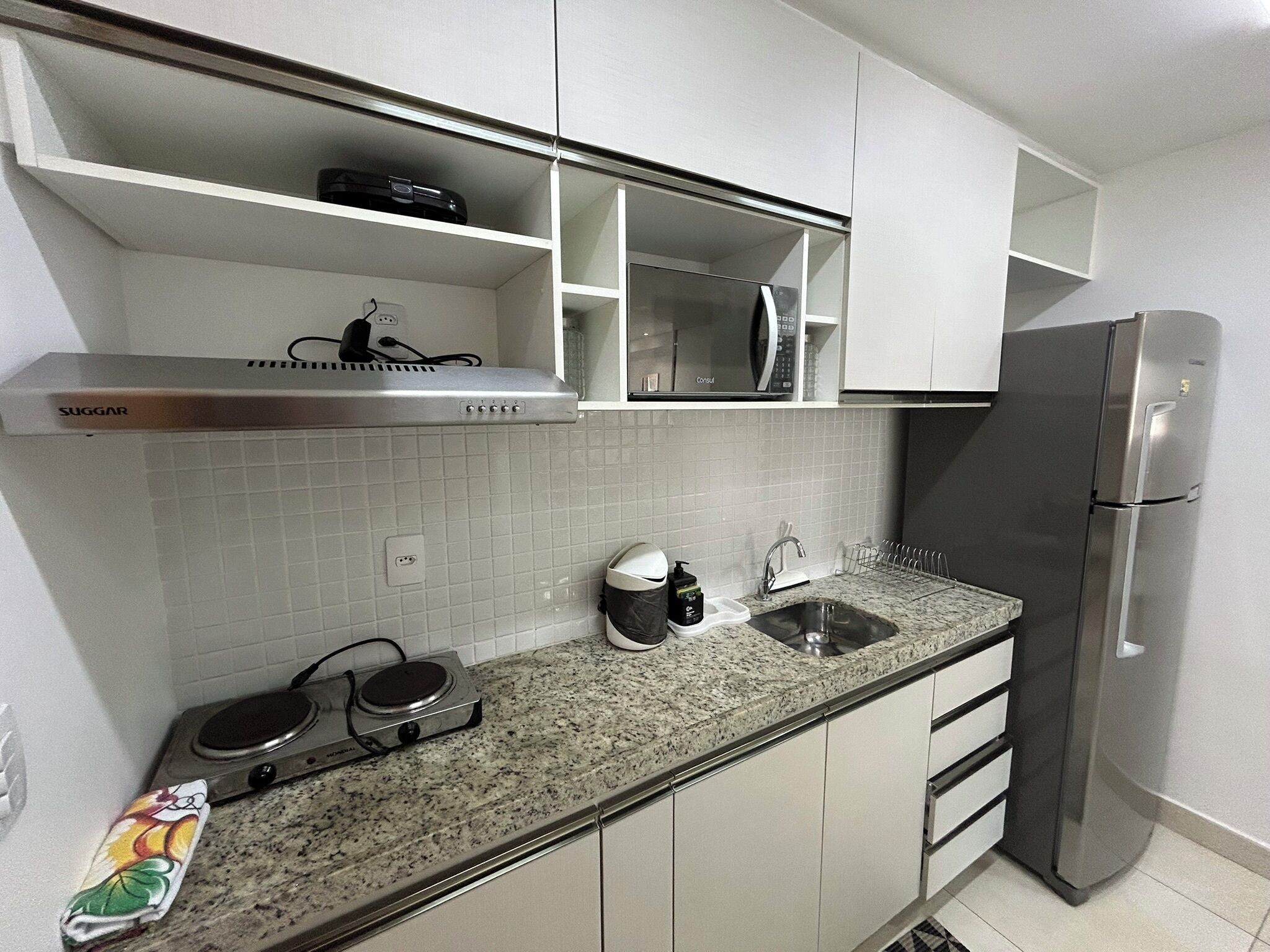 Uma cozinha moderna com armários brancos, uma geladeira de aço inoxidável, um micro-ondas e um fogão a gás.