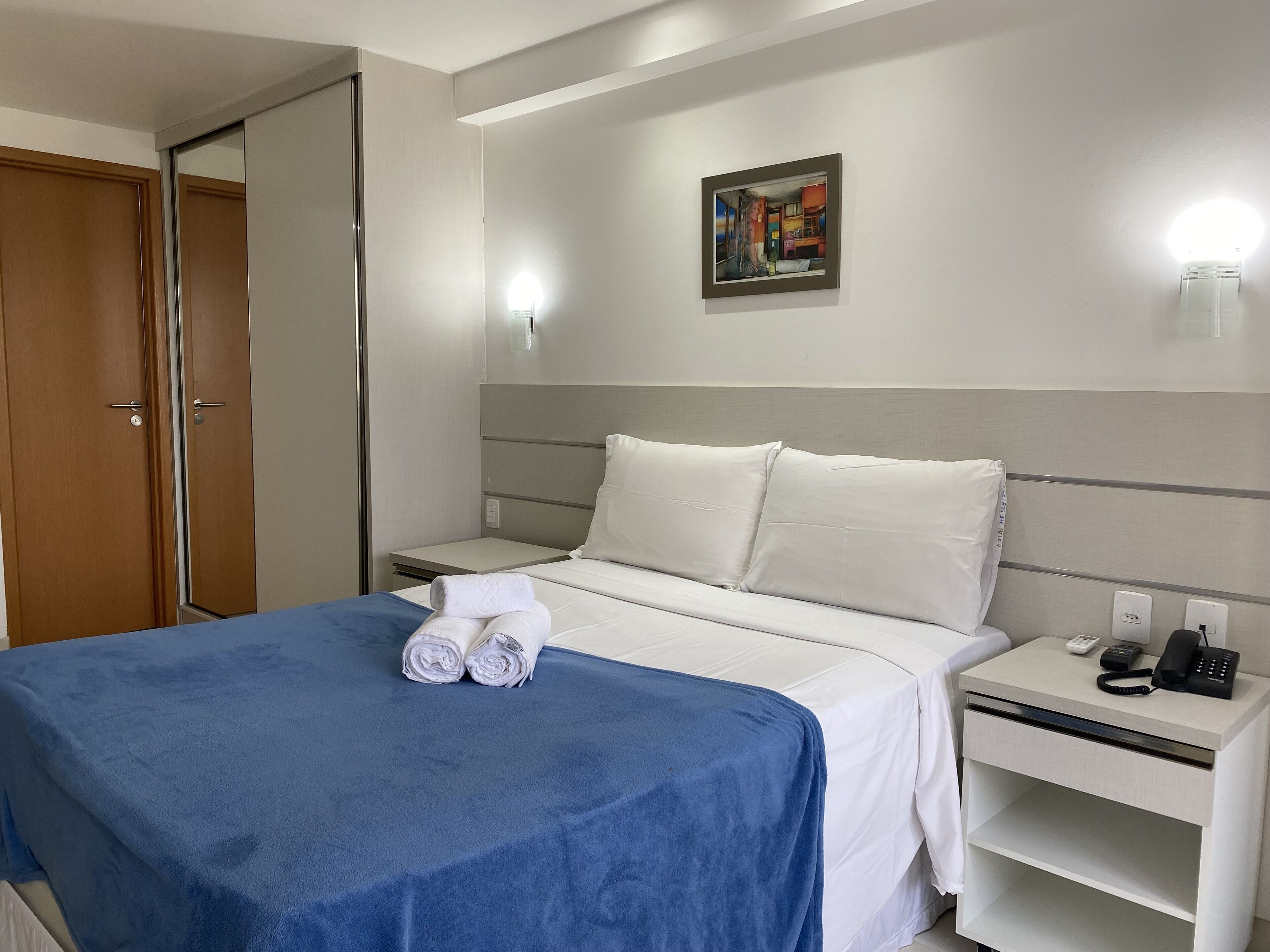 A hotel room with a bed, a nightstand, a phone, and a painting on the wall.