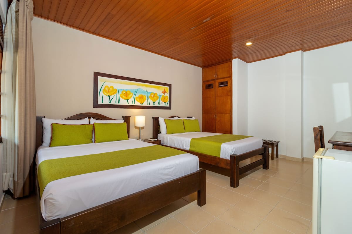 A hotel room with two beds, wooden headboards, a painting on the wall, and a desk with a chair.