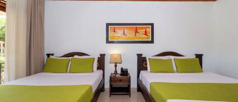 A hotel room with two beds, each with green bedding, a nightstand with a lamp, and a framed painting above the beds.