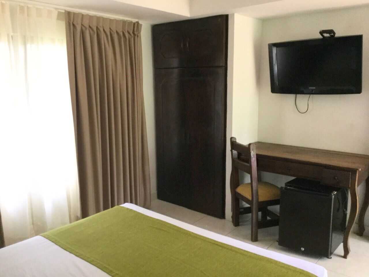 Una habitación de hotel con cama, escritorio, silla, televisor y armario.