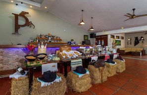 Un espace bar avec un assortiment de bouteilles et de collations, une grande décoration en forme de « P » sur le mur, et des bottes de foin sur lesquelles sont posés des chapeaux.