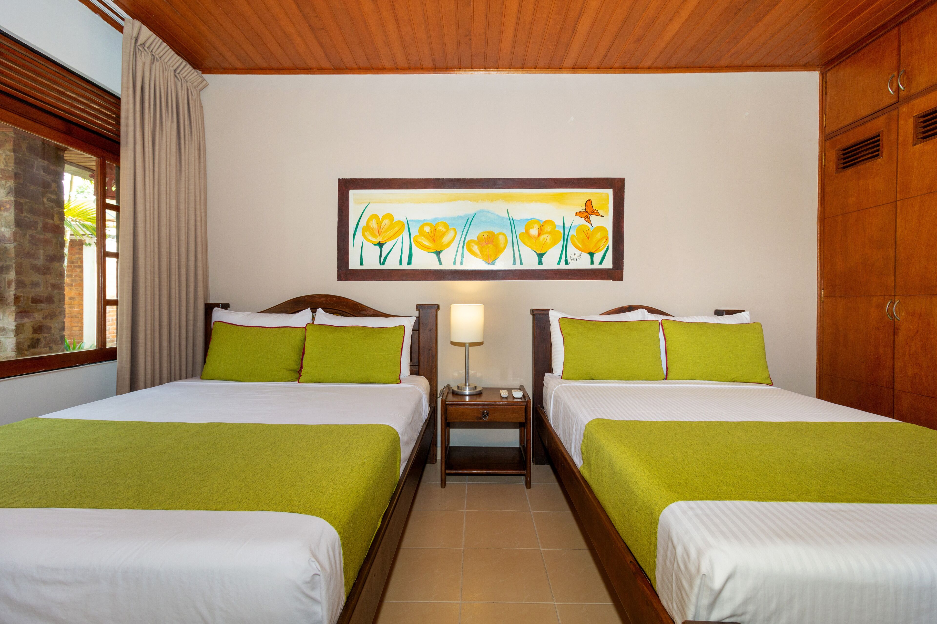 Habitación de hotel con dos camas, una mesita de noche con lámpara, un cuadro en la pared y armarios de madera.
