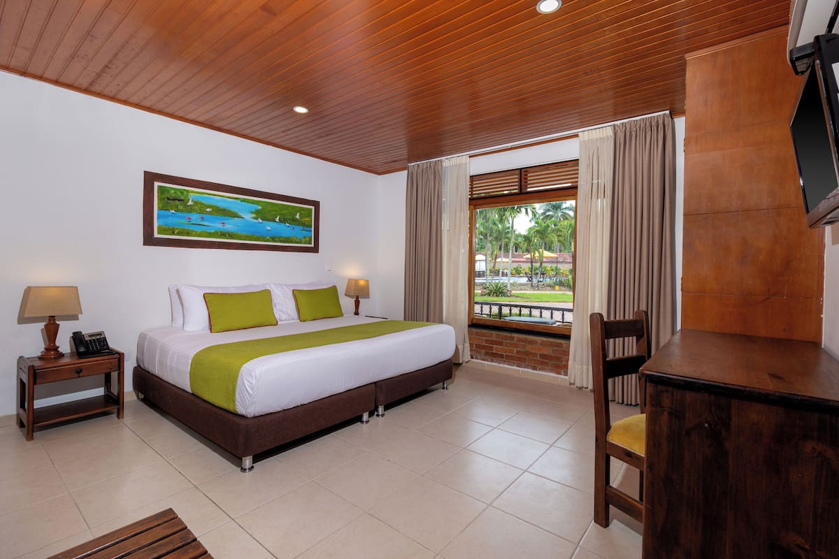 A hotel room with a bed, a desk, a chair, a TV, a window with curtains, and a painting on the wall.