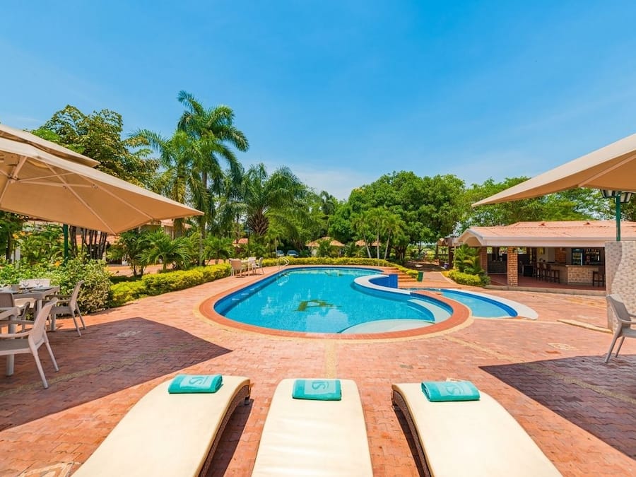 Ein Pool mit Liegestühlen und Sonnenschirmen, umgeben von Grünpflanzen und einem Pflasterweg.
