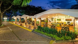 A well-lit outdoor dining area with multiple tables and chairs, surrounded by potted plants and a brick pathway. - Hotel Campestre La Potra (Villavicencio)