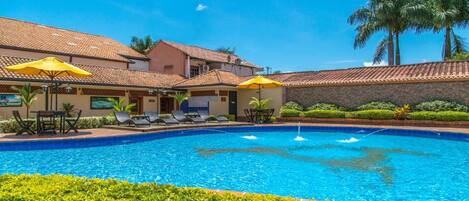 A swimming pool with lounge chairs and umbrellas, surrounded by greenery and palm trees.
