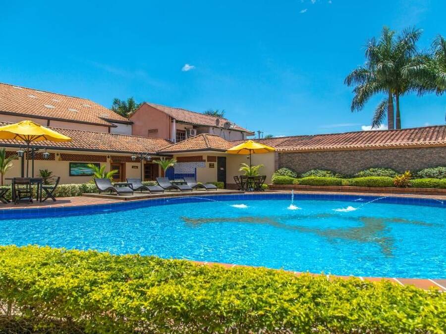 Una piscina con sillas de descanso y sombrillas, rodeada de follaje y palmeras.