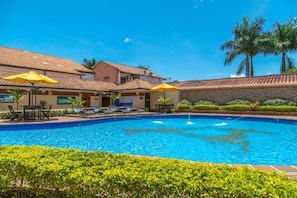 A swimming pool with lounge chairs and umbrellas, surrounded by greenery and palm trees.
