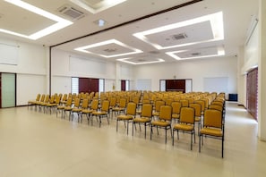 A large conference room with rows of yellow chairs, white walls, and a high ceiling with recessed lighting.