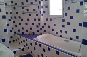 Casa de banho com banheira, janela e azulejos azuis e brancos.