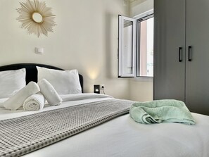 A neatly made bed with white linens, a grey textured throw blanket, and a green towel on the side. - CK Amazing apartment view acropole big terrace (Kallithea)