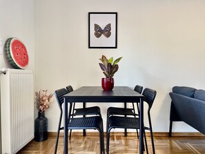 Un comedor con una mesa, sillas, una planta en maceta, un cuadro enmarcado y una tajada de sandía en la pared.