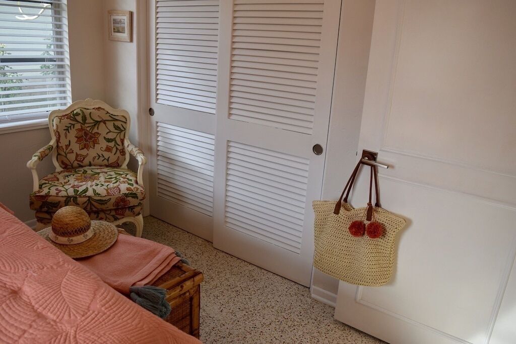 Une pièce comprenant un lit, une chaise, une porte et un sac fixé au mur.