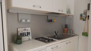 A compact kitchen with white cabinets, a gas stove, a sink, and a small shelf with colorful cups.