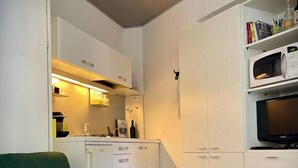 A compact living space with a green sofa, white cabinetry, a microwave, and a television.