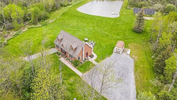 A house with a large yard, a pond, and solar panels.