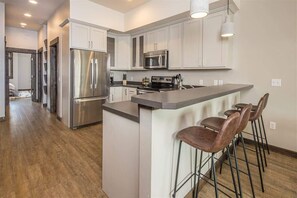 A modern kitchen with stainless steel appliances, a central island with bar stools, and white cabinetry.