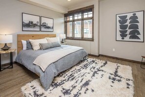 A bedroom with a large bed, two bedside tables with lamps, a window with a view, and artwork on the walls.