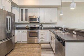 A modern kitchen with stainless steel appliances, white cabinetry, and a built-in dishwasher. - Modern Luxury 1 Bedroom Condo Big Sky Town Center (Big Sky)