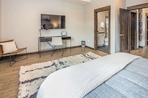 A modern bedroom with a large bed, a desk with a chair, a TV, and a wardrobe. - Modern Luxury 1 Bedroom Condo Big Sky Town Center (Big Sky)