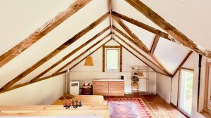 A room with a sloped ceiling, wooden beams, a bed, a dresser, a window, and a rug.