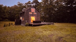 A rustic wooden cabin with a porch and a large window, surrounded by trees.