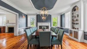 Een eetkamer met een houten tafel en groene fauteuils, een kroonluchter en een open haard.