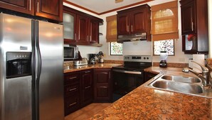 A kitchen with dark wooden cabinets, stainless steel appliances, granite countertops, and a built-in oven. - Amazing Ocean View atop Coco Cliffs (Playa del Coco)