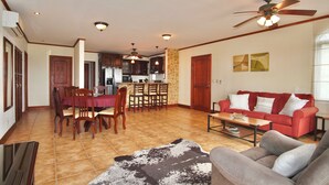 A spacious living area with a red sofa, a coffee table, and a dining table with chairs. There is a kitchen in the background with a stone accent wall. - Amazing Ocean View atop Coco Cliffs (Playa del Coco)