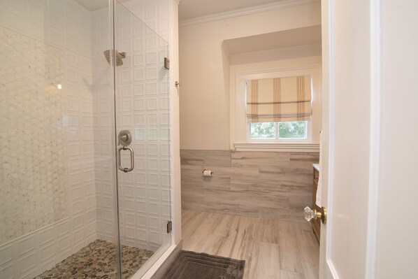 A modern bathroom with a glass shower enclosure, a wooden floor, and a window with a plaid curtain.