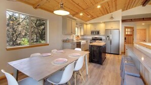 A modern kitchen with wooden beams, a dining area with a table set for four, and a view of trees outside.