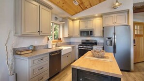 A modern kitchen with light-colored cabinets, stainless steel appliances, and a wooden ceiling.