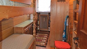 Una stanza in legno compatta con un letto a castello, un tavolino, una sedia, un aspirapolvere e una finestra con tende.