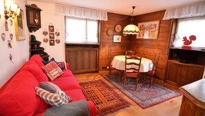 Un accogliente soggiorno con un divano rosso, pareti in legno, un tavolo da pranzo con sedie e una televisione.