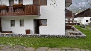Un edificio bianco con un balcone, gradini in pietra e un'area verde con fiori.