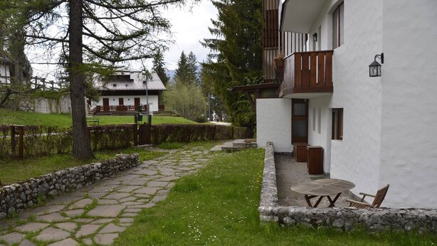 Un vialetto in pietra conduce a un edificio bianco con un balcone e posti a sedere all'aperto.
