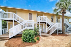 A building with multiple white staircases leading to balconies, a palm tree, and a well-maintained garden area. - Beach Service Included, Sandpiper Cove 2005! (Destin)