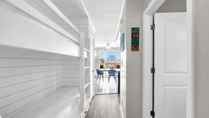 A hallway with white walls and a wooden floor leading to a dining area with blue chairs and a table.