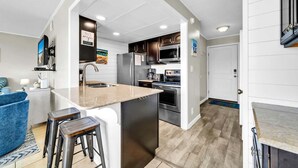 A modern kitchen with a central island, stainless steel appliances, and a blue accent chair.