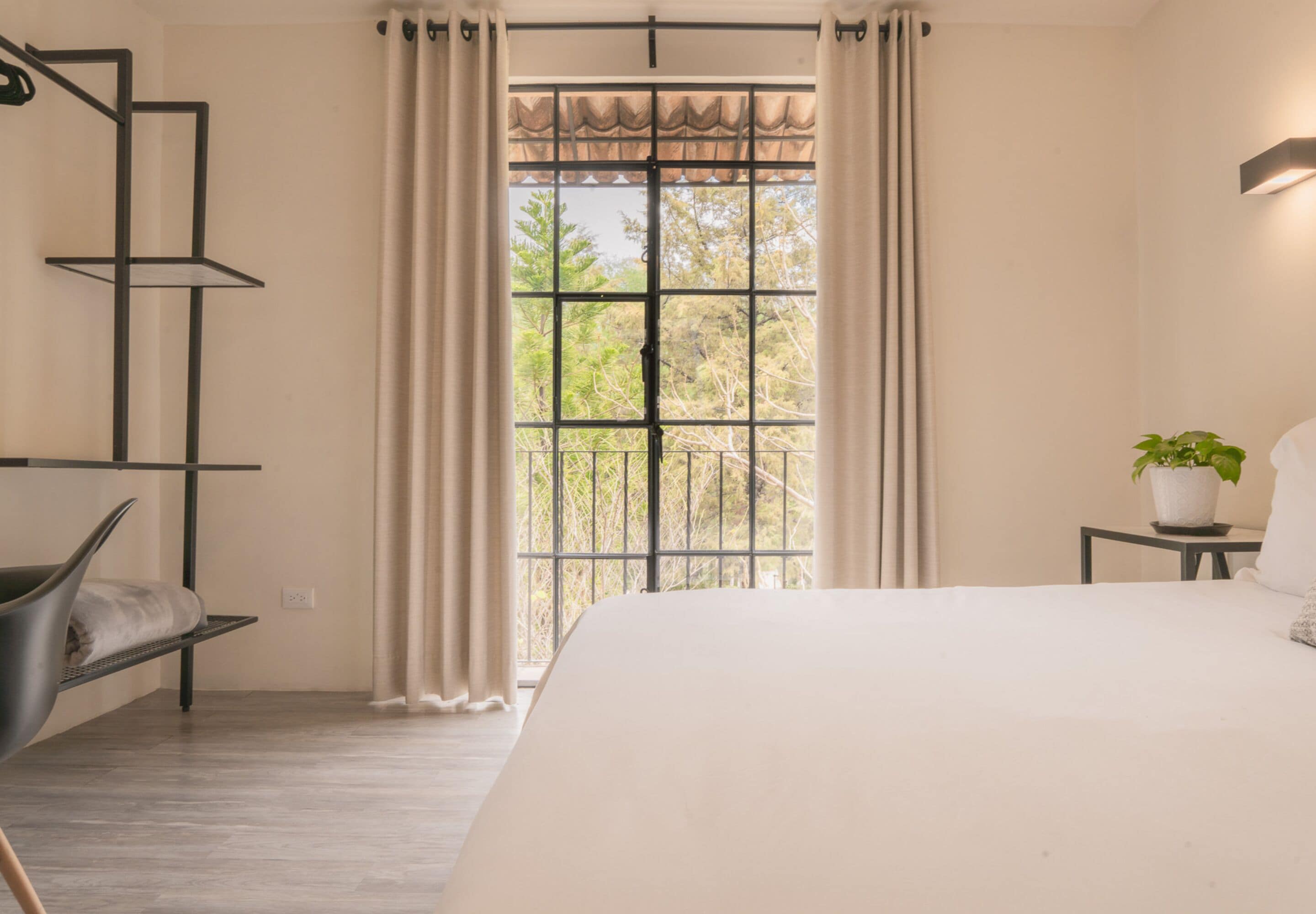 A bedroom with a large bed, a window with curtains, a potted plant, and a chair.