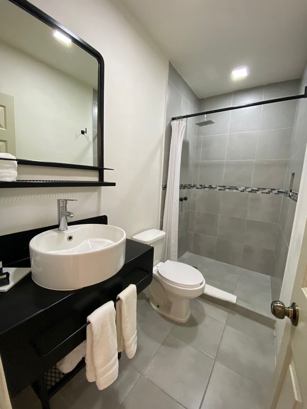 A modern bathroom with a white sink, black countertop, and a glass-enclosed shower.