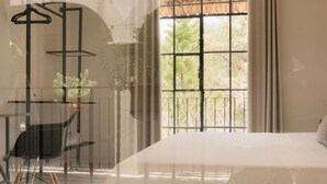 A bedroom with a large window, a bed, a chair, and a table with a hanging plant. - Casa Doper Guadiana (San Miguel de Allende)