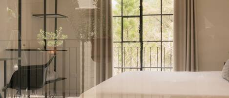 A bedroom with a large window, a bed, a chair, and a table with a hanging plant.